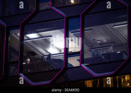 Tallinn, Estland - 03. Januar 2025: Ansicht der geometrischen Wabenfenster, die die starken Leuchtstofflampen des Innenraums reflektieren, während eine Einzelfigur ist Stockfoto