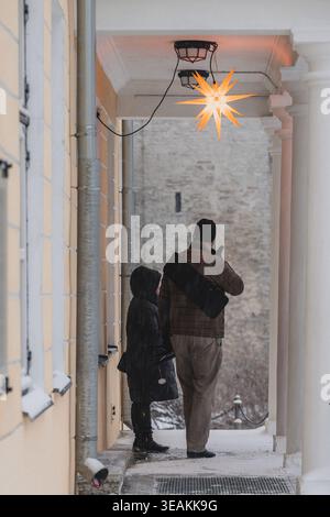 Tallinn, Estland - 03. Januar 2025: Blick auf einen Vater und ein Kind, die unter einem beleuchteten Stern stehen und auf die alten Steinmauern der Altstadt auf einem schneebedeckten Boden blicken Stockfoto