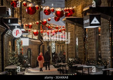 Tallinn, Estland - 03. Januar 2025: Blick auf die kopfsteingepflasterten Straßen der Altstadt, die mit festlichen roten Ornamenten und funkelnden Lichtern geschmückt sind, als Fußgänger Stockfoto