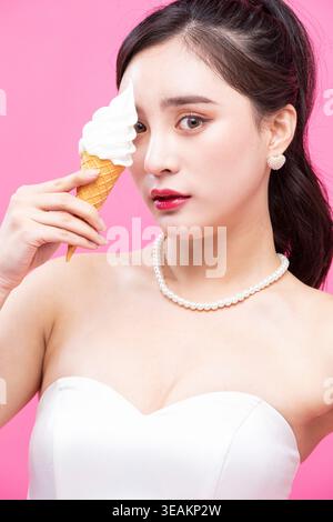 Eine Frau hält einen schmelzenden Eiskegel vor einem hellrosa Hintergrund. Stockfoto