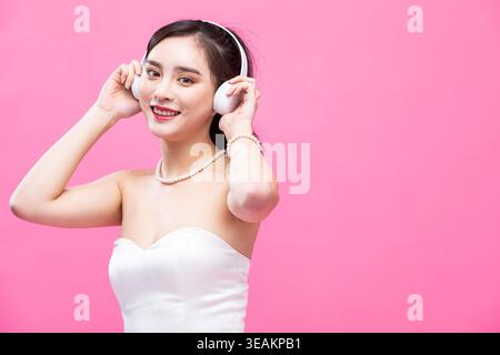 Eine junge Frau in einem weißen Hochzeitskleid lächelt und trägt weiße Kopfhörer. Stockfoto