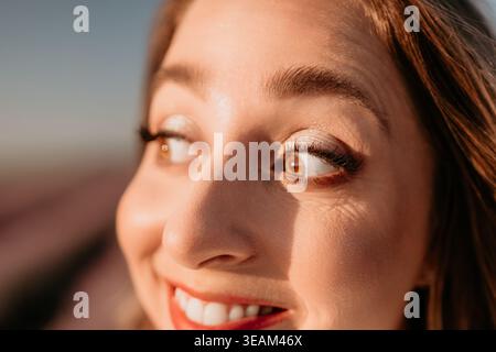 Porträtfrau Lächeln Sie eine glückliche junge Frau, die während des Lichtes der goldenen Stunde wegschaut Stockfoto