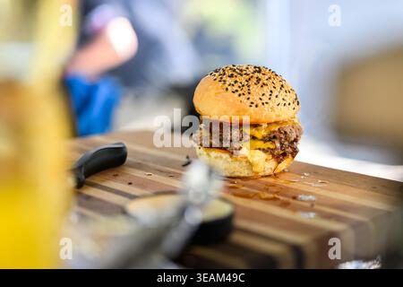 Nahaufnahme eines frisch zubereiteten Cheeseburgers mit doppelten Rindfleischpasteten, geschmolzenem Käse und Sesambrötchen auf einer Holzoberfläche, die saftig ist Stockfoto
