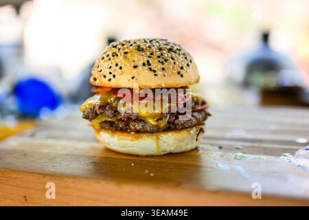 Nahaufnahme eines frisch zubereiteten Cheeseburgers mit doppelten Rindfleischpasteten, geschmolzenem Käse und Sesambrötchen auf einer Holzoberfläche, die saftig ist Stockfoto