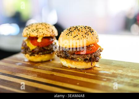 Nahaufnahme eines frisch zubereiteten Cheeseburgers mit doppelten Rindfleischpasteten, geschmolzenem Käse und Sesambrötchen auf einer Holzoberfläche, die saftig ist Stockfoto