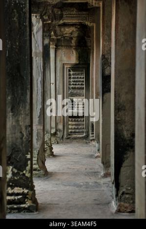 Schmaler stimmungsvoller Steinkorridor in einem Angkor-Tempel in Kambodscha mit alten geschnitzten Wänden und dunkler stimmungsvoller Atmosphäre. Stockfoto