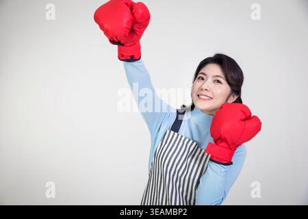 Eine junge Frau mit Kochmütze und Schürze, Boxhandschuhe und Lächeln, steht in einer Küche. Stockfoto