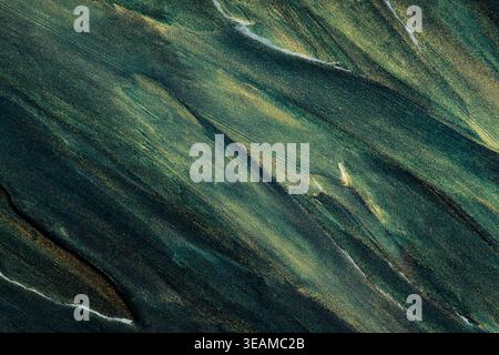 Abstrakte Ölfarbe mit Glitzer, die schräg fließende grüne und goldene Muster erzeugt Stockfoto