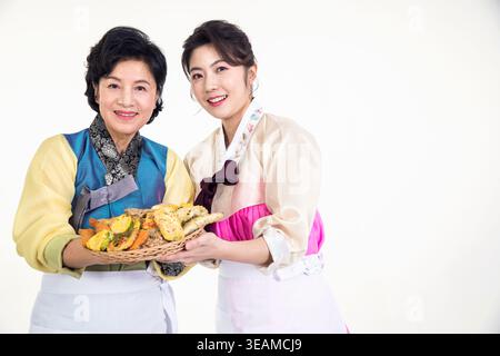 Zwei Frauen, eine ältere und eine junge Frau, lächeln und halten einen Korb voll mit koreanischen Pfannkuchen. Stockfoto