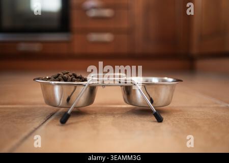 Tierschalen aus Metall mit Trockenfutter auf dem Küchenboden. Konzept der Tierpflege, der Fütterungsroutine und der häuslichen Lebensweise. Futter für Katzen oder Hunde. Stockfoto