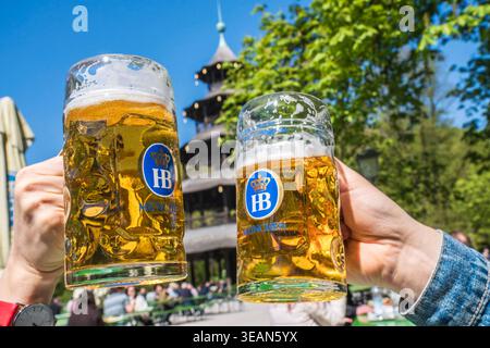 Biergarten am Chinesischen Turm, Frühlingstag im Englischen Garten, zwei Gäste stoßen mit Ihrer Mass Bier an, München, April 2026 Deutschland, München, 22. April 2026, Biergarten am Chinesischen Turm, Frühling im Englischen Garten, Temperaturen bis 16 Grad, viele genießen die Sonne bei Bier und einer Brotzeit, zwei Gäste staßen mit ihren Masskrügen an, alles ist grün, Mittwochmittag, Bayern *** Biergarten am Chinesischen Turm, Frühlingstag im Englischen Garten, zwei Gäste stoßen mit ihren Bierbecher an, München, April 2026 Deutschland, München, 22. April, 2026, Biergarten am Chinesischen Turm, Frühling Stockfoto
