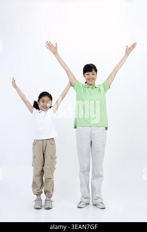 Mutter und Tochter stehen zusammen, Arme zur Feier hoch, auf weißem Hintergrund. Stockfoto