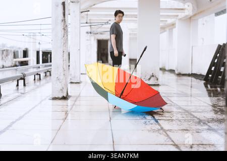 Farbenfroher Schirm auf der Bahnsteig mit einem jungen Mann im Hintergrund, stimmungsvoll Stockfoto