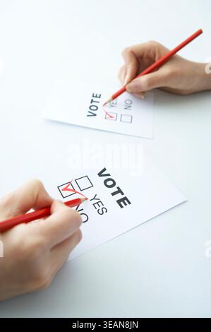 Zwei Hände halten rote Bleistifte und füllen identische Stimmzettel mit einem roten Häkchen aus. Stockfoto