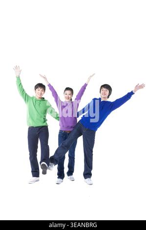 Drei junge asiatische Freunde stehen zusammen, lächeln und heben aufgeregt die Arme. Stockfoto