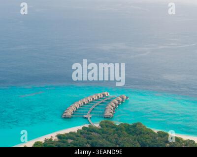 Blick aus der Vogelperspektive auf die Bungalows über dem Wasser, die sich bis ins türkisfarbene Meer erstrecken, von einem grünen Inselparadies, Hoarafushi, Thiladhunmathee Uthuruburi, Malediven. Stockfoto