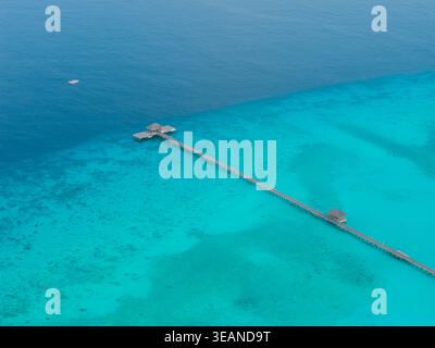 Aus der Vogelperspektive auf einen langen Pier, der sich in das türkisfarbene Meer erstreckt, die Wellen küssen sanft die Küste, Hoarafushi, Thiladhunmathee Uthuruburi, Malediven. Stockfoto
