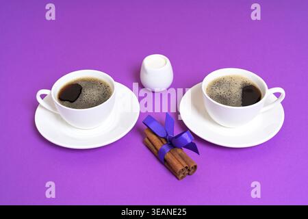 Zwei Kaffeetassen mit Zimtstangen und Milchkännchen auf lila Hintergrund Stockfoto
