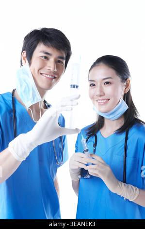 Ein junger asiatischer Arzt und eine junge asiatische Krankenschwester, beide in blauen Peelings, die Spritzen in einem Krankenhaus halten. Stockfoto