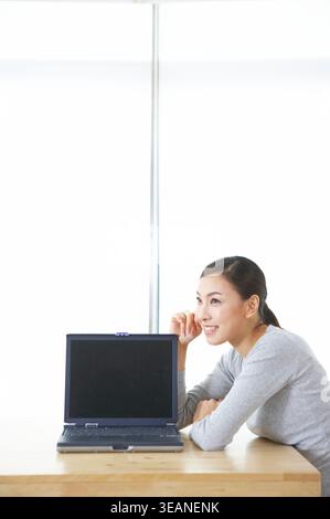 Eine Frau sitzt vor einem Laptop mit leerem Bildschirm. Stockfoto