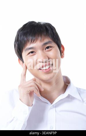 Ein junger asiatischer Mann mit nachdenklichem Ausdruck berührt seine Wange und schaut auf etwas in der Ferne. Stockfoto