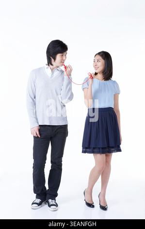 Ein junger Mann und eine junge Frau teilen einen zärtlichen Moment, indem sie einen roten Faden in Herzform austauschen. Stockfoto