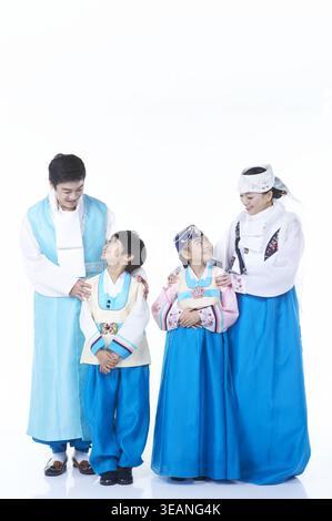 Eine vierköpfige koreanische Familie, darunter zwei Kinder, steht zusammen in Hanbok, lächelt und blickt in die Ferne. Stockfoto