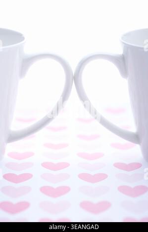 Zwei weiße Kaffeetassen sitzen auf einem Tisch mit Herzdesign und sind bereit, mit Liebe gefüllt zu werden. Stockfoto