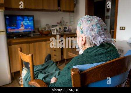 Alte Seniorin allein zu Hause, Fernsehen mit Haarrollen, Einsamkeit im Alter Stockfoto