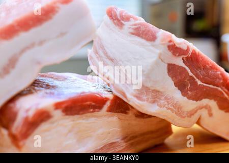 Mehrere Stücke des rohen Schweinebauchs befinden sich auf Holzoberfläche in der Küche bereit für die Zubereitung der Mahlzeiten. Stockfoto