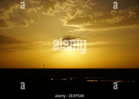 Goldener Sonnenuntergang mit Sonnenstrahlen durchdringenden Wolken über einer ruhigen Feuchtlandschaft Stockfoto