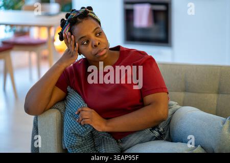 Müde frustrierte afroamerikanische Frau sitzt zu Hause auf dem Sofa und fühlt sich irritiert, verärgert, schlecht gelaunt Stockfoto
