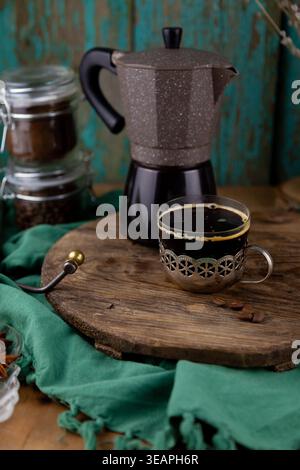 Frisch gebrühter Espresso im Vintage Glasbecher mit Geysir-Kaffeemaschine auf rustikalem Holzbretthintergrund. Trinken Sie in einem alten Becherhalter aus Metall Stockfoto