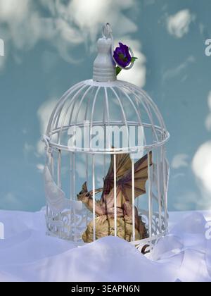 Ein Spielzeugdrache in einem romantischen Vogelkäfig. Stockfoto