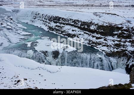 Isländischer schneebedeckter Wasserfall und gefrorener Fluss in der Winter Canyon Landschaft Stockfoto