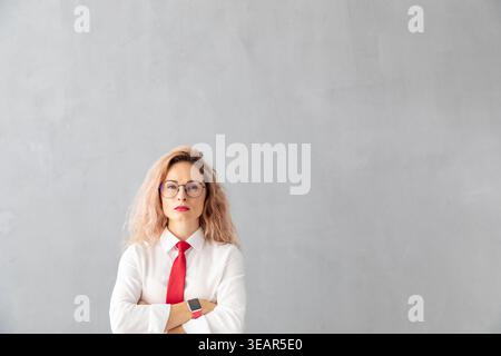 Erfolgreiche junge Geschäftsfrau im Büro. Frau, die drinnen vor grauem Wandhintergrund mit Kopierraum steht Stockfoto