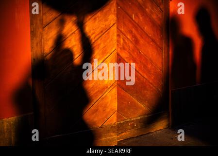 Verschwommene Silhouetten von Menschen, die auf eine warme, farbige Wand mit starker Beleuchtung gegossen werden. Abstrakte urbane Szene geeignet für Konzepte der Interaktion, Bewegung, A Stockfoto