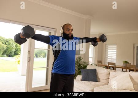 Afroamerikaner, der zu Hause seitlich hochfährt, hält Hexen-Kurzhanteln in blauem Sportshirt. Gewichte, Workout, Fitness, Kraft, Training, sh Stockfoto