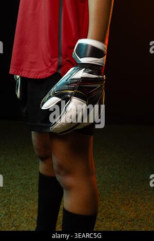 Afroamerikanische Torhüterin aus rotem Jersey mit gepolstertem Handschuh und Handgelenkriemen auf dem Rasen. Athlet, Fußball, Studio, Felgenbeleuchtung, Nahaufnahme, Ar Stockfoto