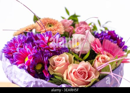 Ein lebendiger Blumenstrauß aus verschiedenen frischen Blumen in lila Papier, ein durchdachtes Geschenk Stockfoto