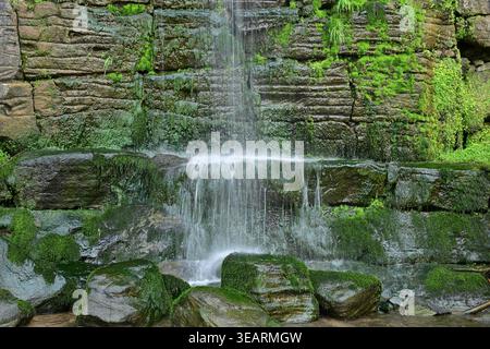 Sanfter moosiger Wasserfall, der über felsige Waldklippen fällt Stockfoto