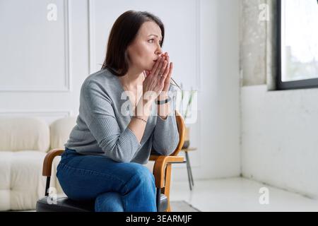 Depressive, besorgte reife Frau, die auf einem Stuhl sitzt, zu Hause Stockfoto