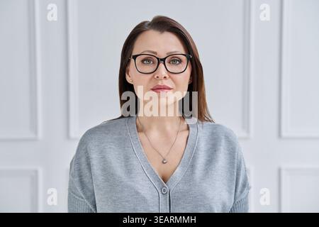 Kopfporträt einer Brille tragenden Frau mittleren Alters, die auf weißem Hintergrund in die Kamera blickt Stockfoto