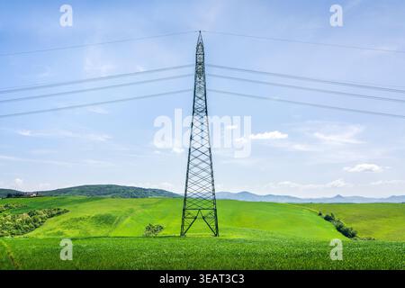 Hochspannungsturm in einem üppigen grünen Feld in der Toskana. Moderne Infrastruktur in einer ländlichen Frühlingslandschaft bei Volterra, Italien Stockfoto
