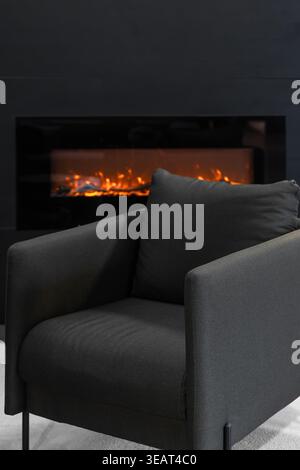 Eleganter dunkelgrauer Sessel in der Nähe des Kamins. Moderne Inneneinrichtung für den Wohnbereich. Stockfoto
