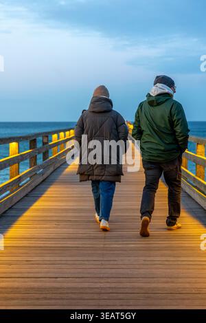 Ein paar, das auf einem Holzsteg läuft. Abendspaziergang am Meer. Stockfoto