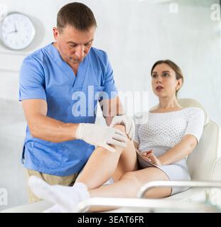 Frau, die sich über Beinschmerzen beim Chirurgen in der Klinik beschwert Stockfoto