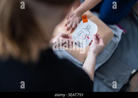 Die Person führt während des ersten-Hilfe-Kurses an der Trainingskuppe eine HLW-Thoraxkompression durch. AED-Pads und Rettungsausrüstung liegen in der Nähe, was den Notfall hervorhebt Stockfoto
