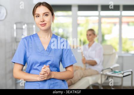 Selbstbewusste lächelnde Schönheitschirurgin, die in der Arztpraxis steht Stockfoto
