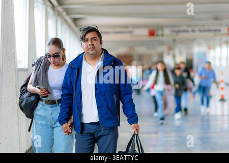 Mann und Frau, die Hände halten, gehen durch eine Bushaltestelle in Mexiko und bereiten sich auf eine gemeinsame Inlandsreise vor. Stockfoto